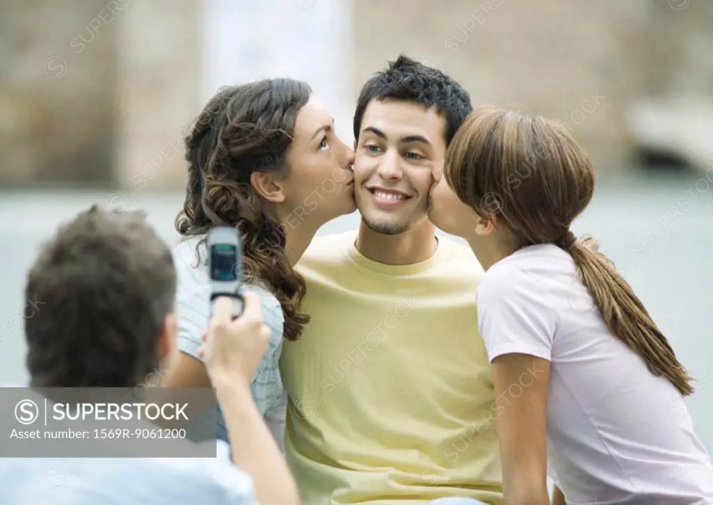 Teen girls kissing boy´s cheeks while second boy takes photo