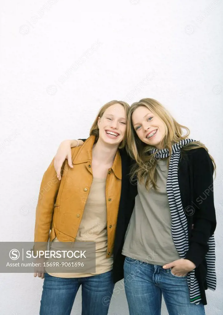 Two young female friends, one with arm around the other´s shoulders, both smiling at camera