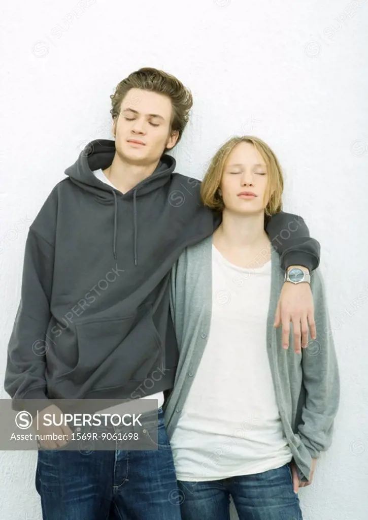 Young couple leaning against wall, man´s arm around woman´s shoulder, both closing eyes