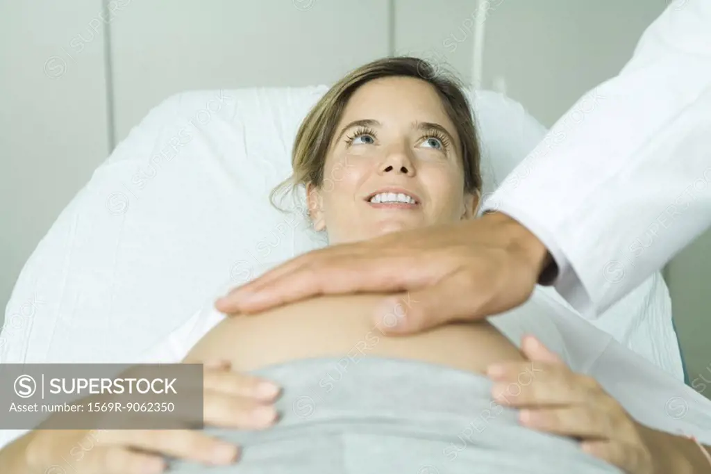 Pregnant woman lying on back in doctor´s office, doctor´s hand on woman´s stomach