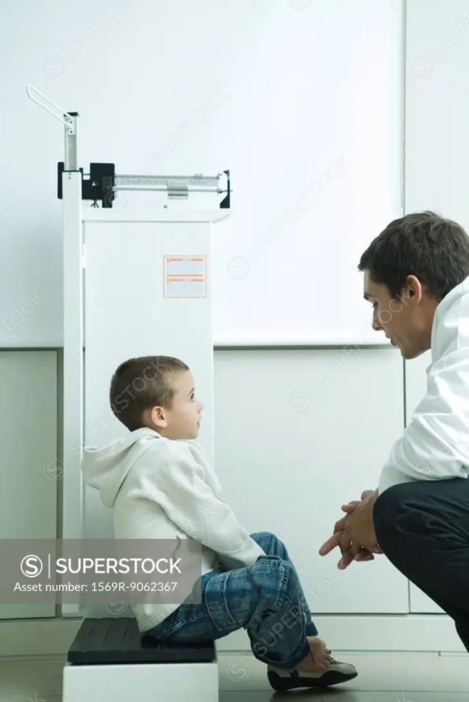 Boy sitting on scale talking to doctor in doctor´s office