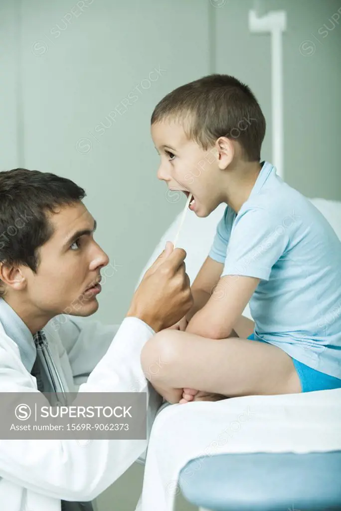 Doctor looking into boy´s mouth with tongue depressor, side view