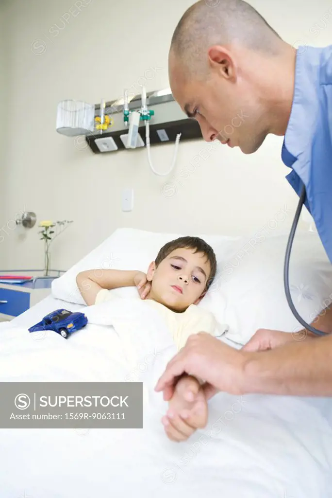 Boy lying in hospital bed, intern holding boy´s arm