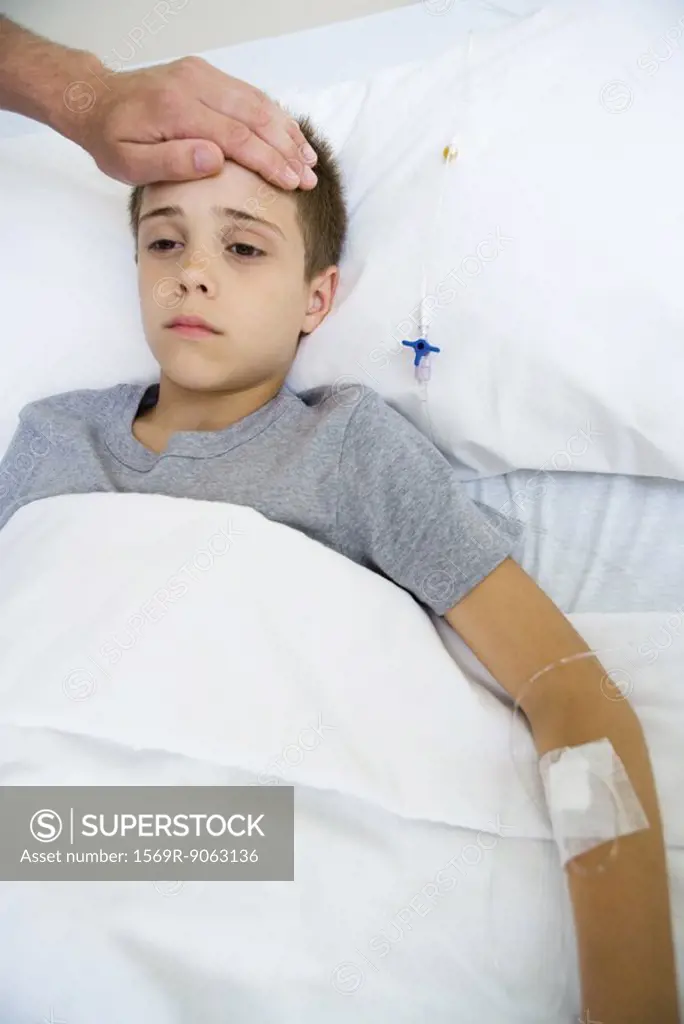 Boy lying in hospital bed, man´s hand on boy´s forehead