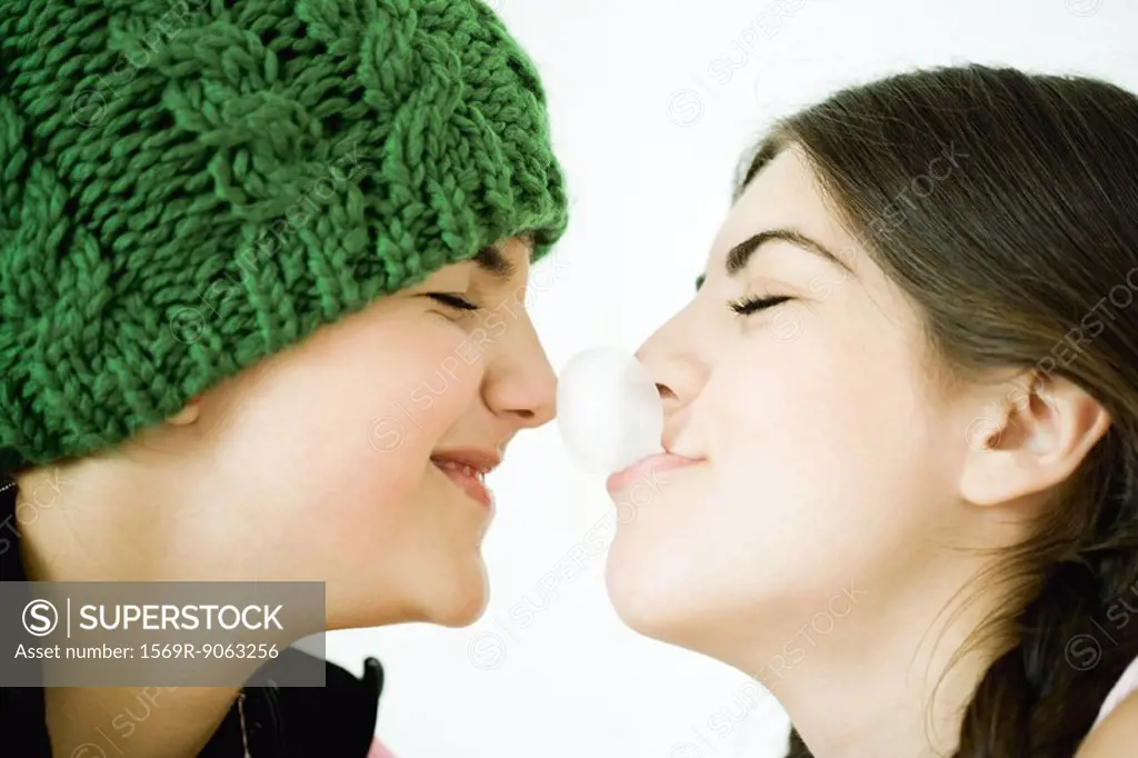Two young female friends, one blowing bubble with gum, touching friend´s nose