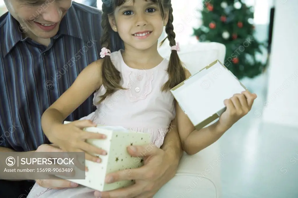 Girl sitting on father´s lap holding Christmas present