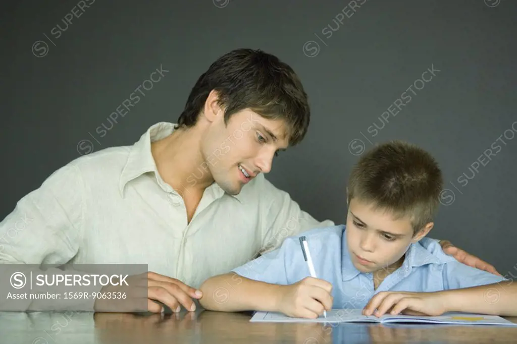Father and son, man looking over boy´s shoulder as he does homework