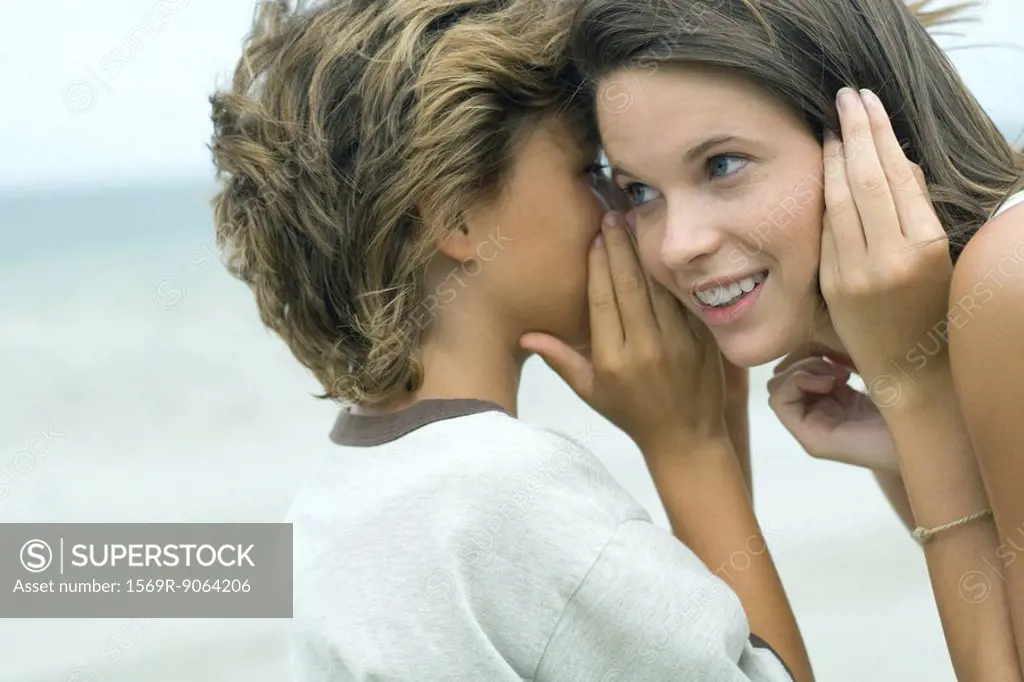 Boy whispering in teen sister´s ear, close-up