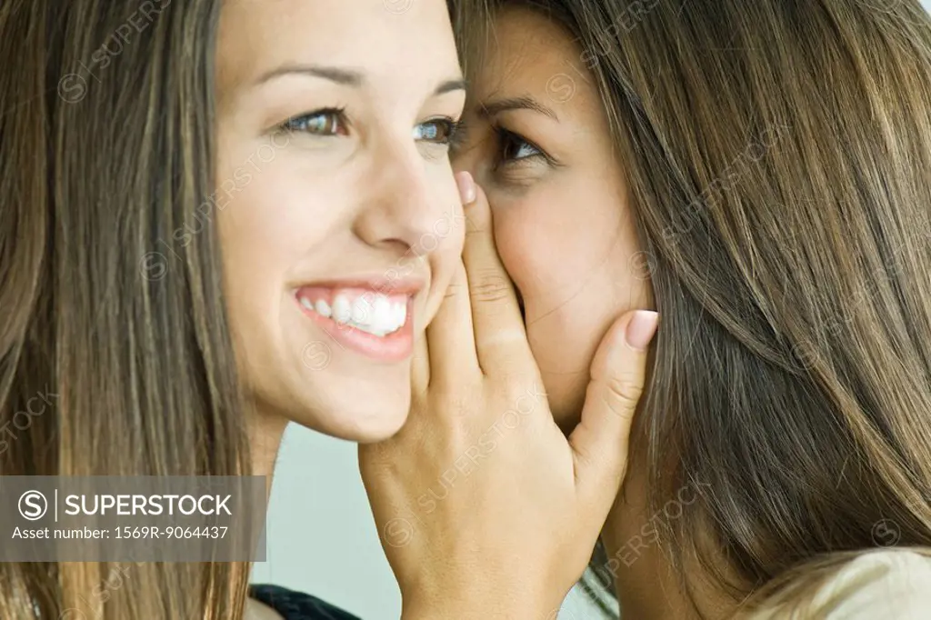 Teenage girl whispering in twin sister´s ear, close-up