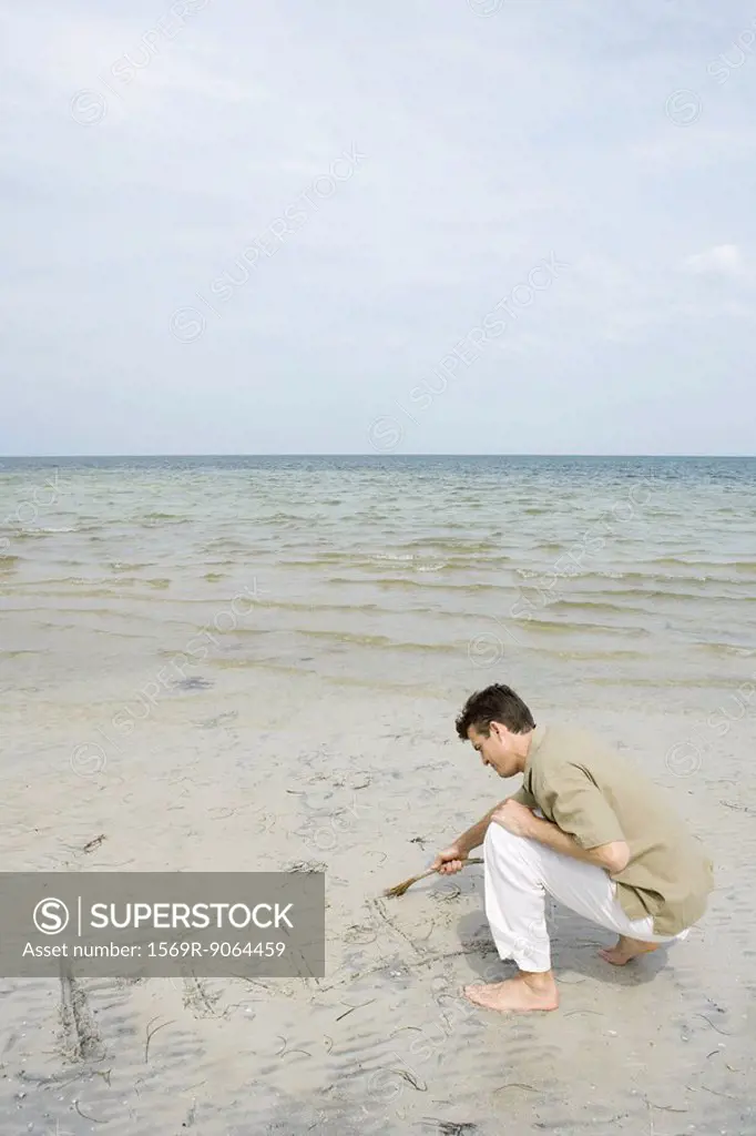 Man crouching on beach writing the word ´free´ in sand with a stick