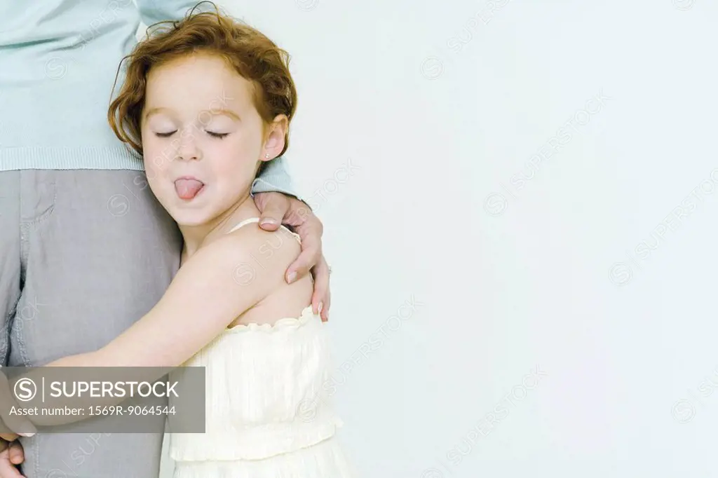 Little girl holding on to mother´s leg, sticking tongue out at camera