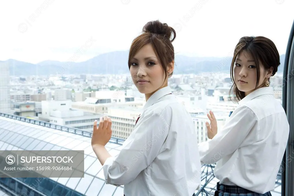 Young females standing in front of window, looking over shoulders at camera