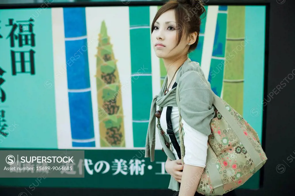 Young female walking past large poster with Japanese script, side view