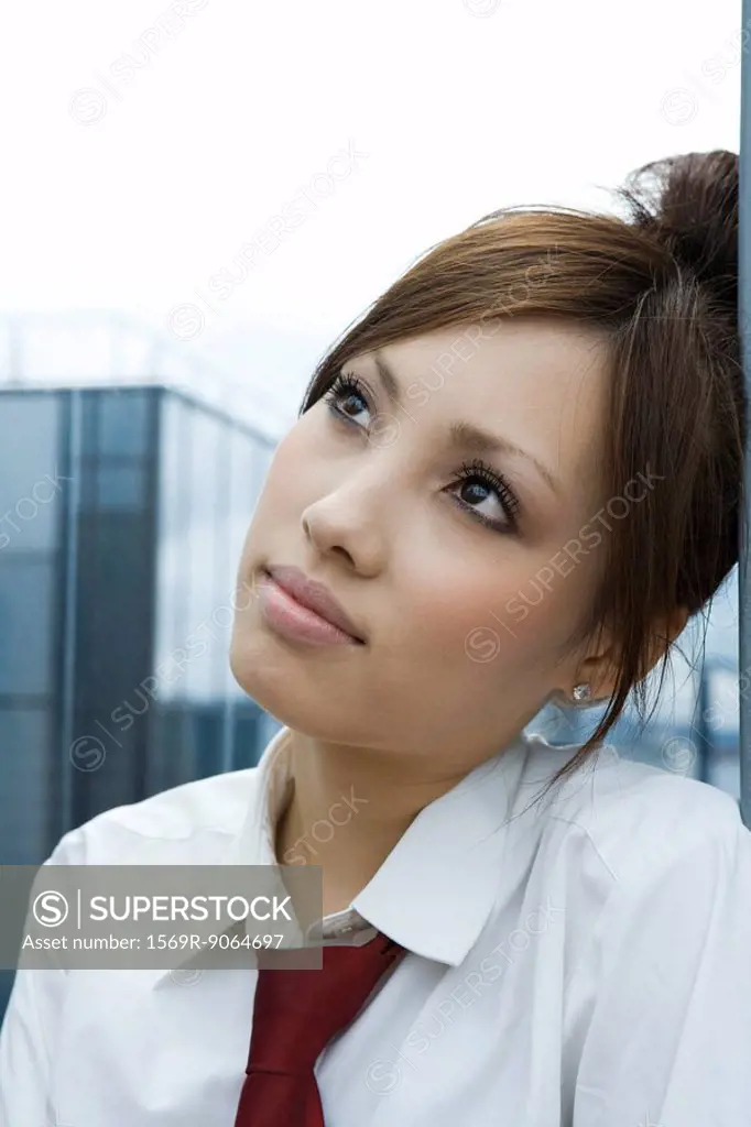 Young female leaning head against wall, looking up, portrait
