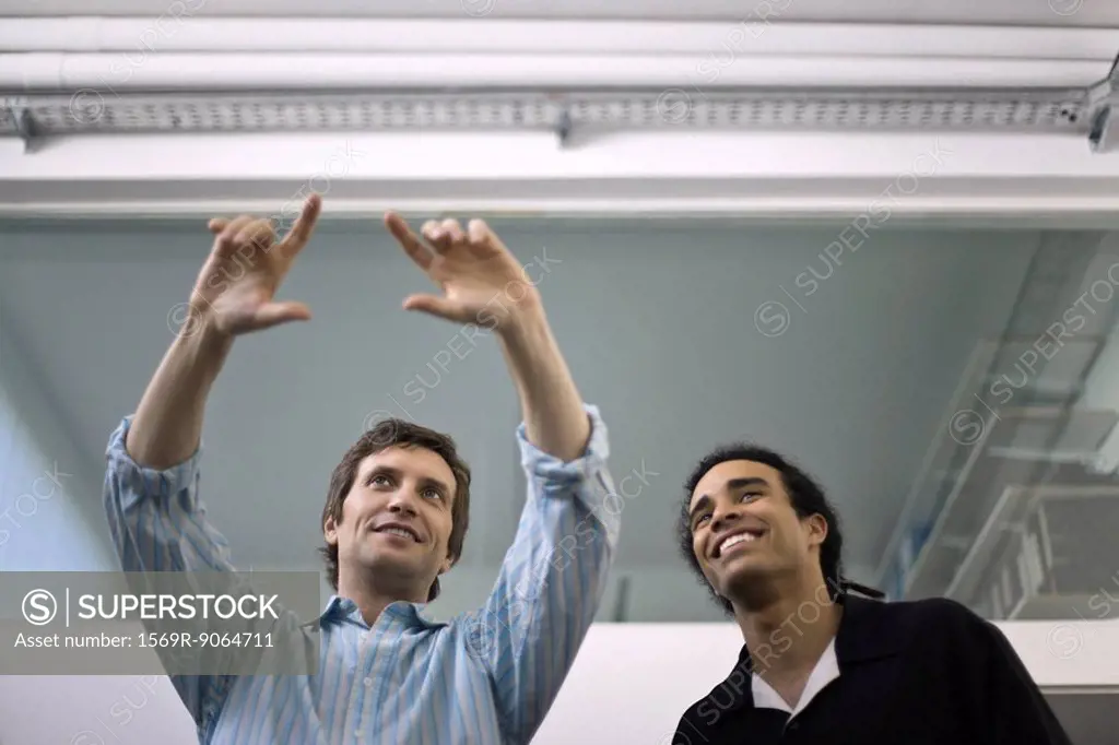 Man making gesture, explaining to colleague looking on