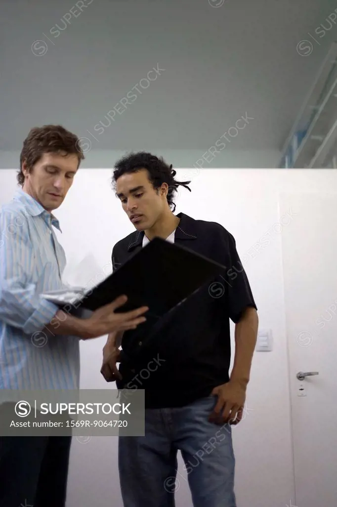 Men standing together looking over contents of binder