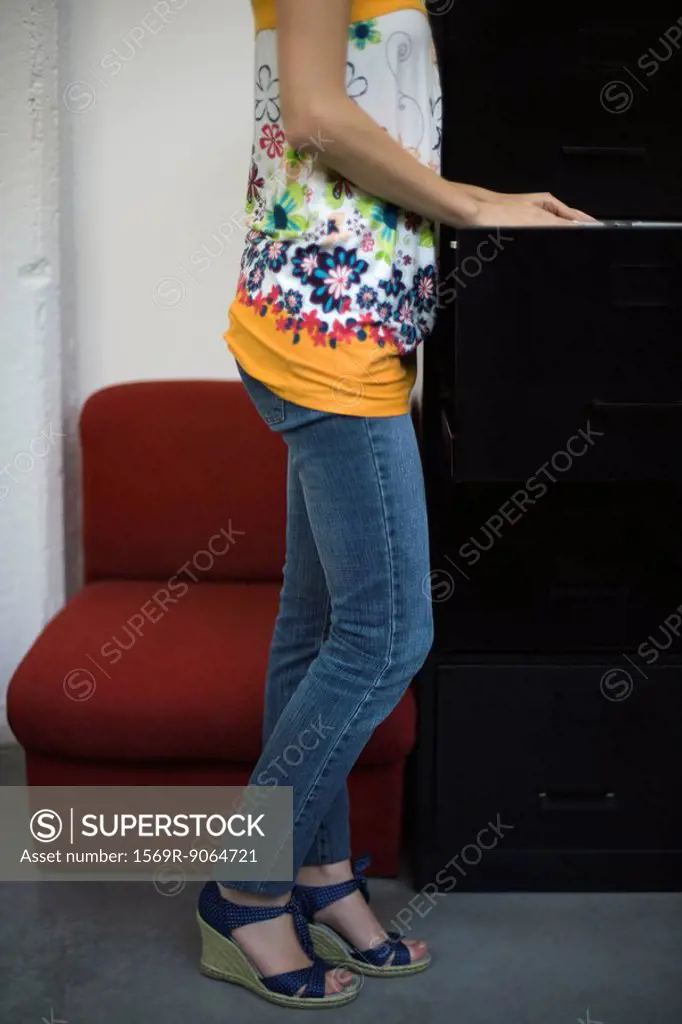 Casually dressed woman looking through filing cabinet, cropped