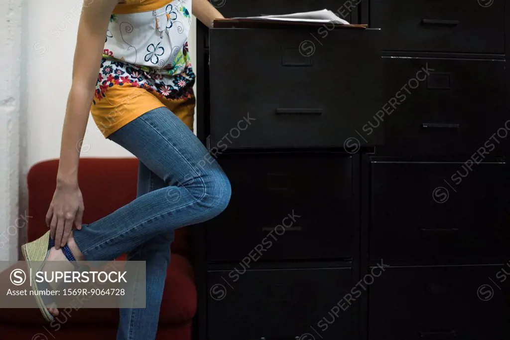 Woman adjusting shoe, leaning against filing cabinet