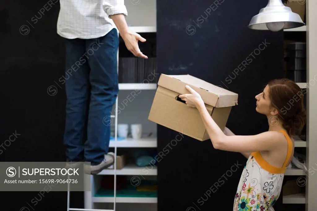 Woman handing box to man standing on ladder