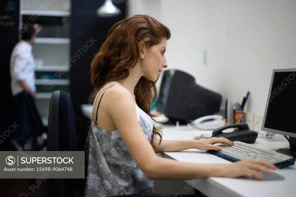 Woman working at desk, colleague standing in background