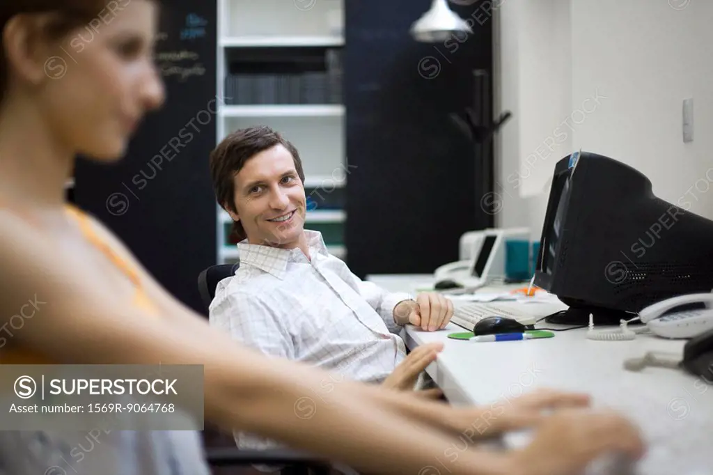 Man sitting at desk, smiling at female colleague