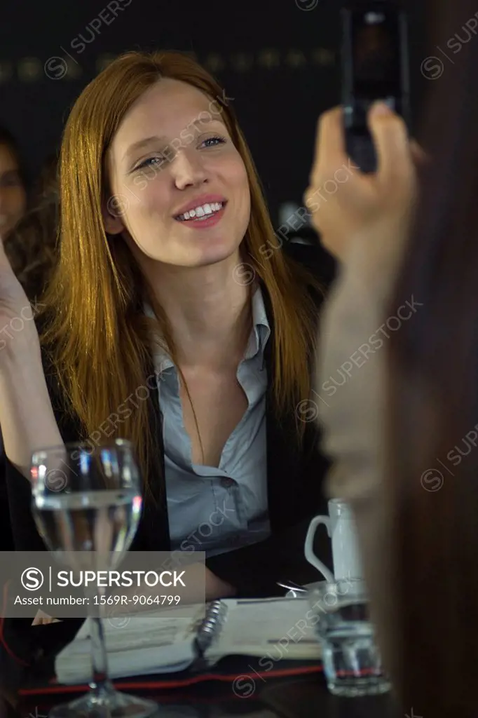 Woman posing for photo taken with cell phone in cafe