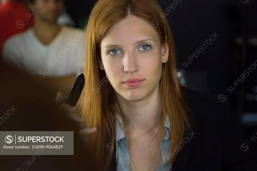 Woman holding cell phone, staring at camera