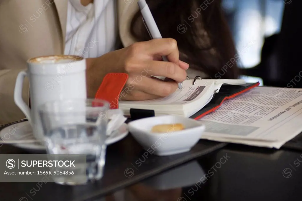 Woman sitting in cafe, writing in agenda, cropped view