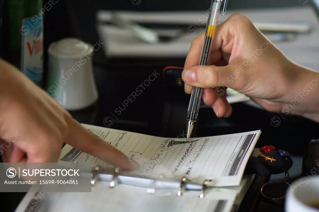 Two people making plans using agenda, one holding pen while the other points to page