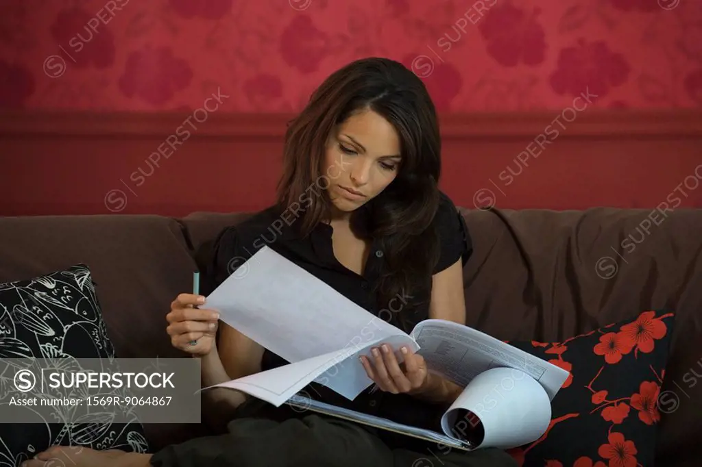 Young woman sitting on sofa, reading document