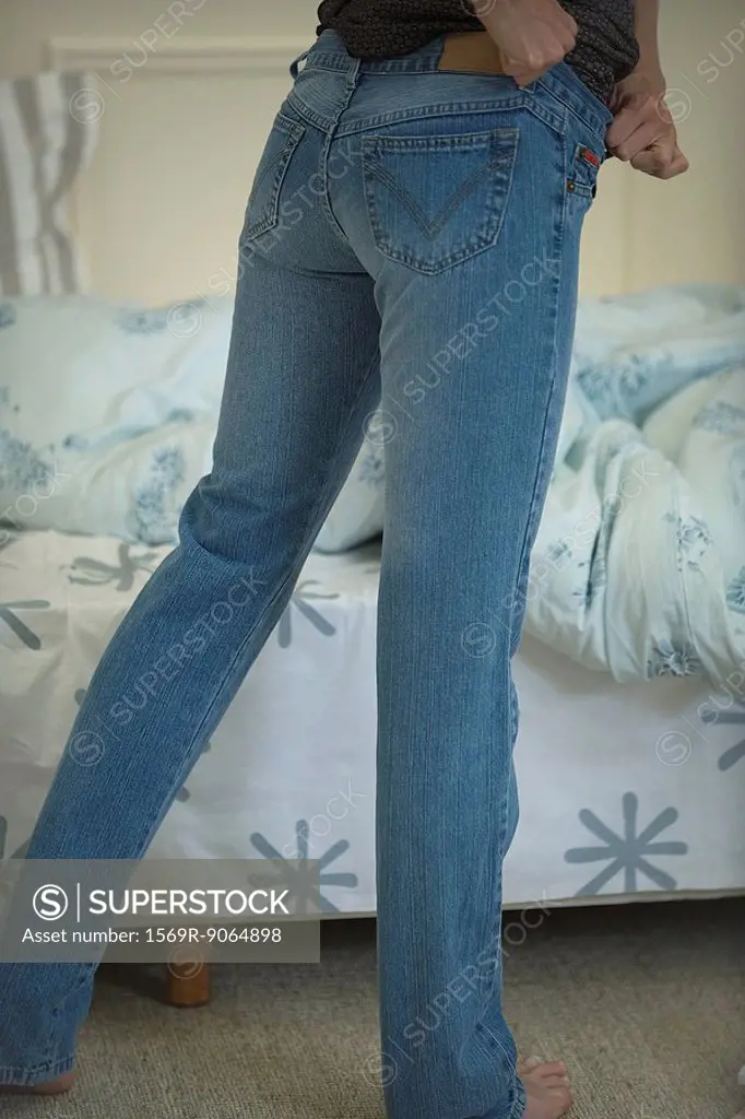 Woman putting on snug-fitting jeans, cropped view