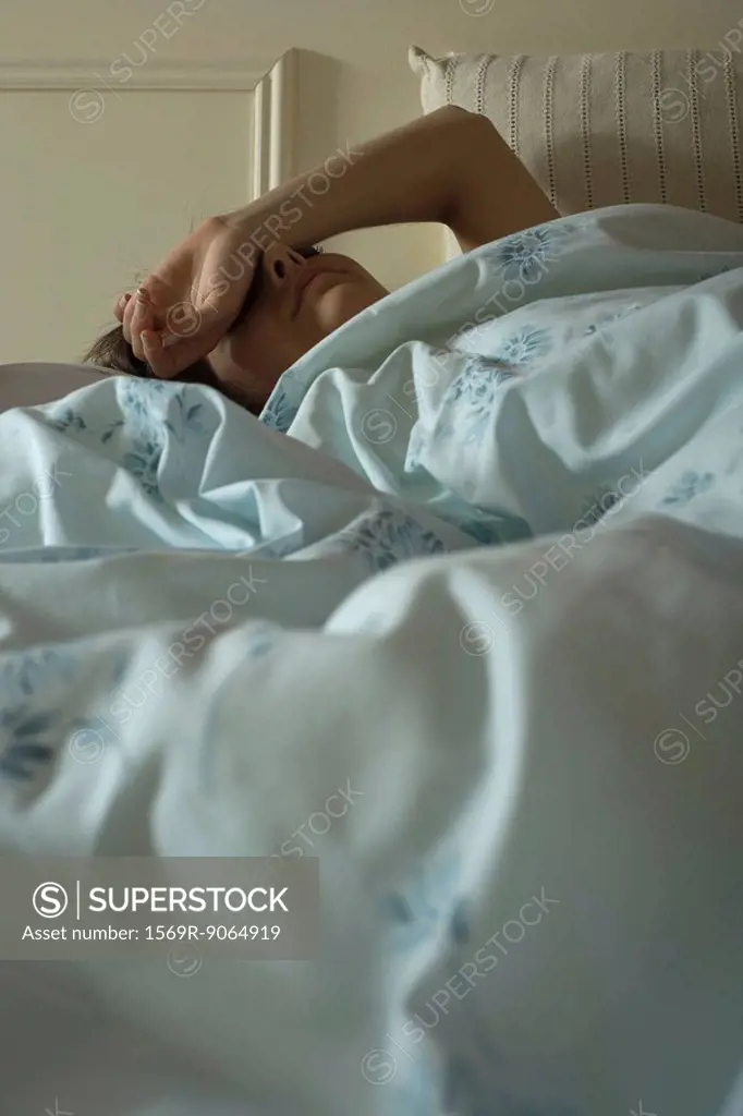 Woman lying in bed with arm over face