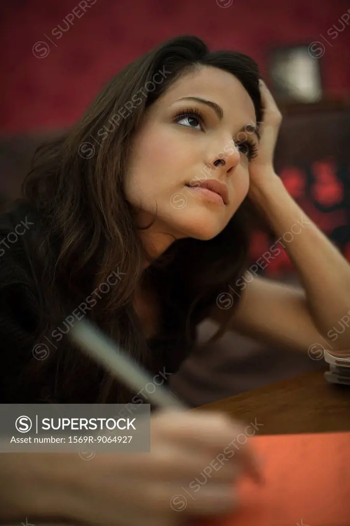 Young woman writing, looking up in thought