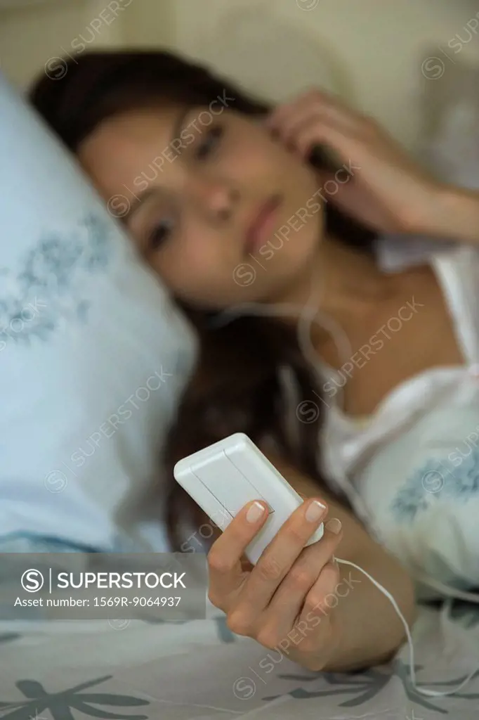 Young woman lying in bed, listening to MP3 player
