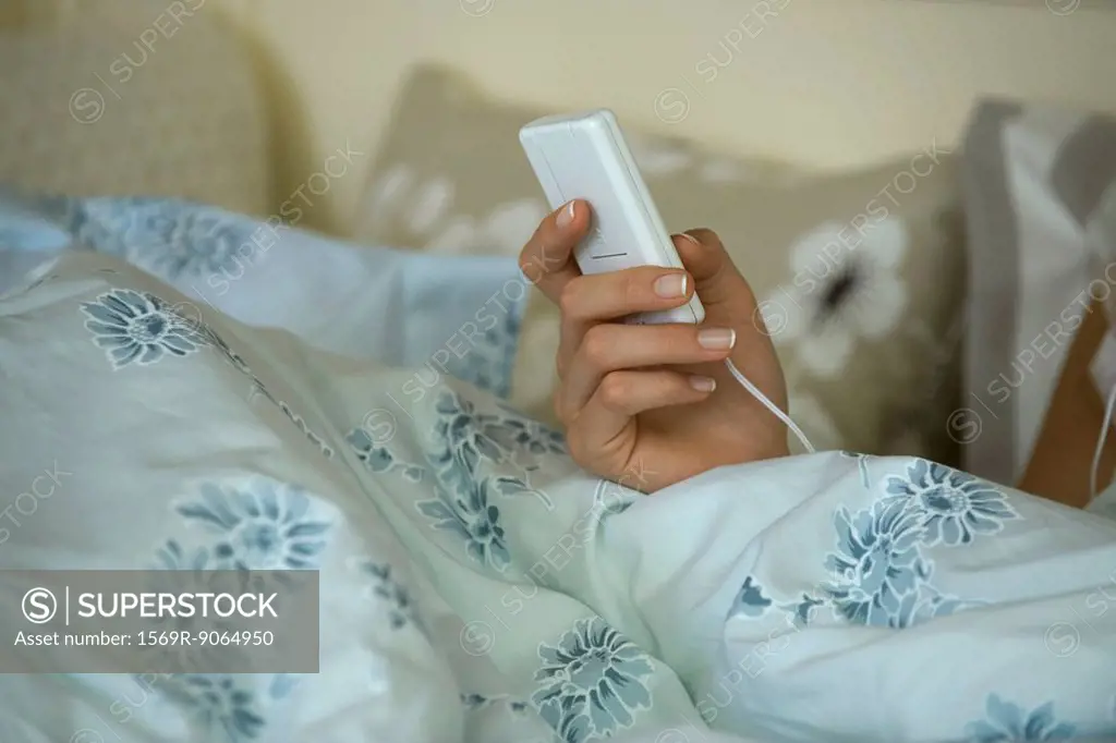 Woman in bed, holding MP3 player, cropped view of hand