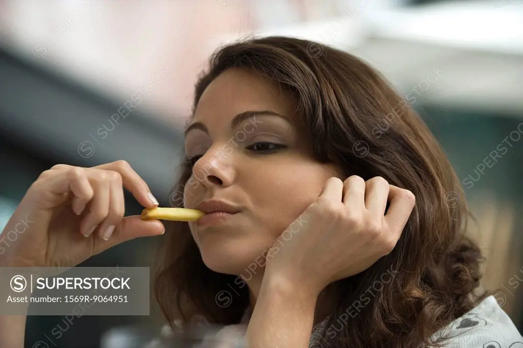 Young woman eating french fries, hand under chin