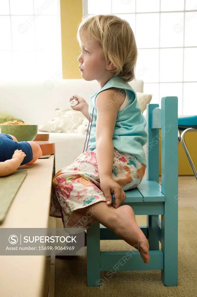 Toddler girl sitting at table, touching ankle, side view