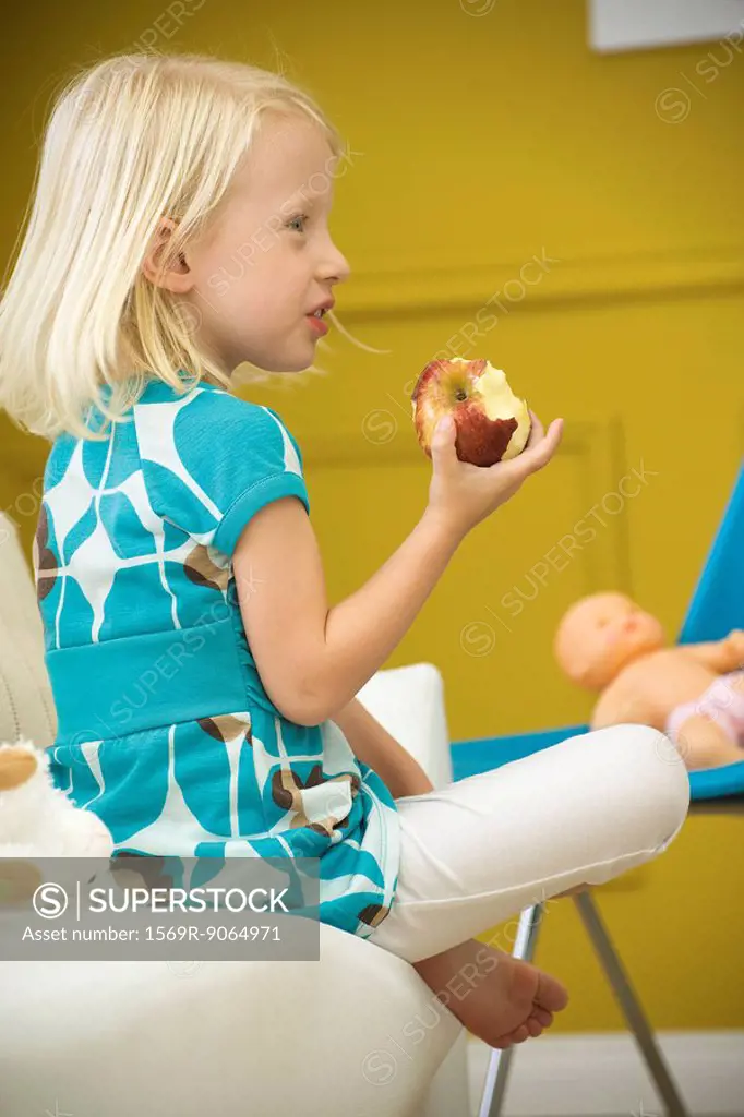Little girl eating apple on sofa, side view