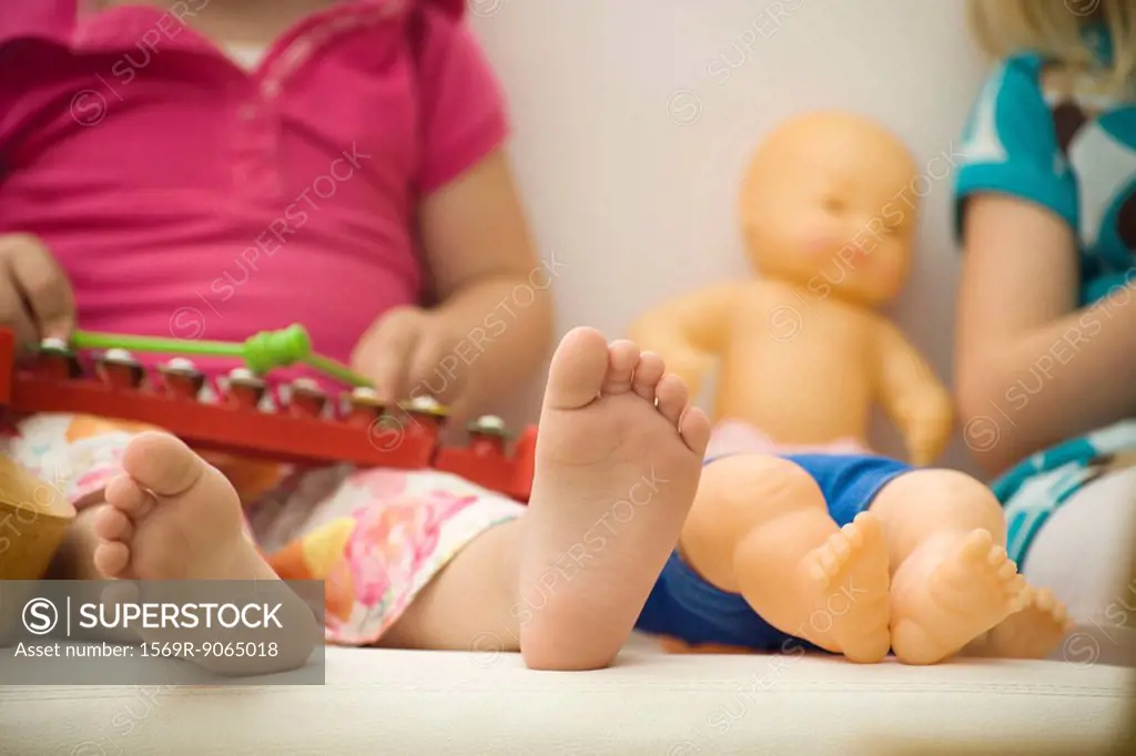 Little girl sitting beside baby doll, close-up of bare feet