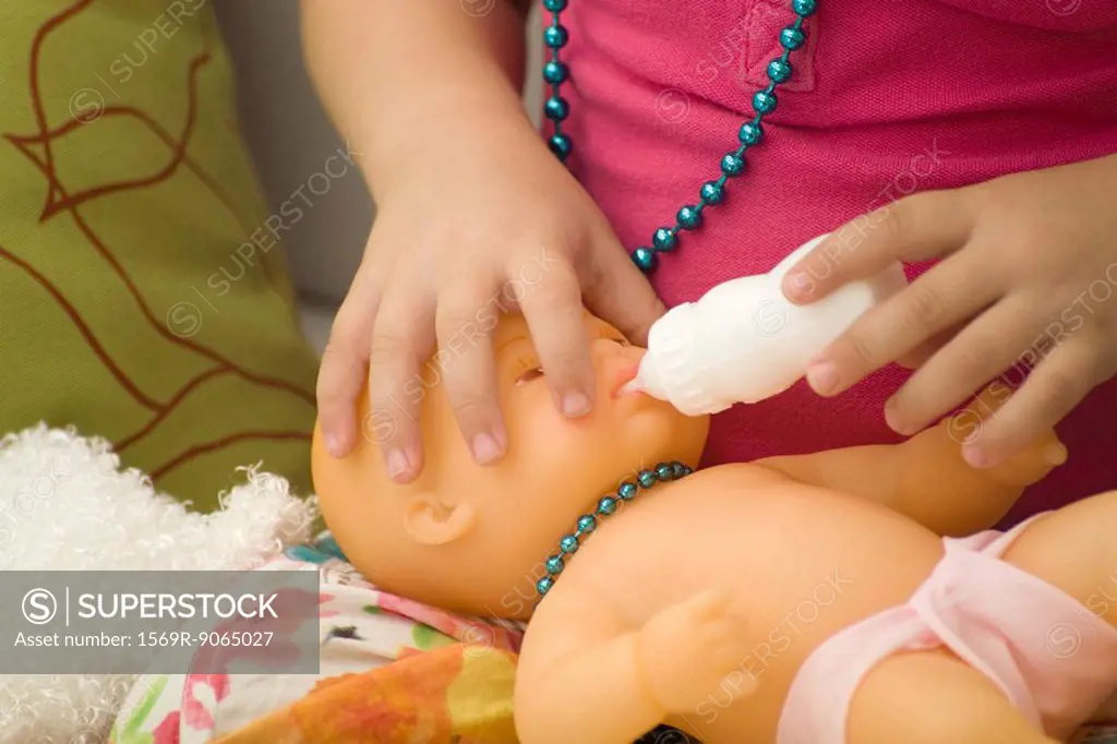 Little girl feeding baby doll with bottle, cropped view