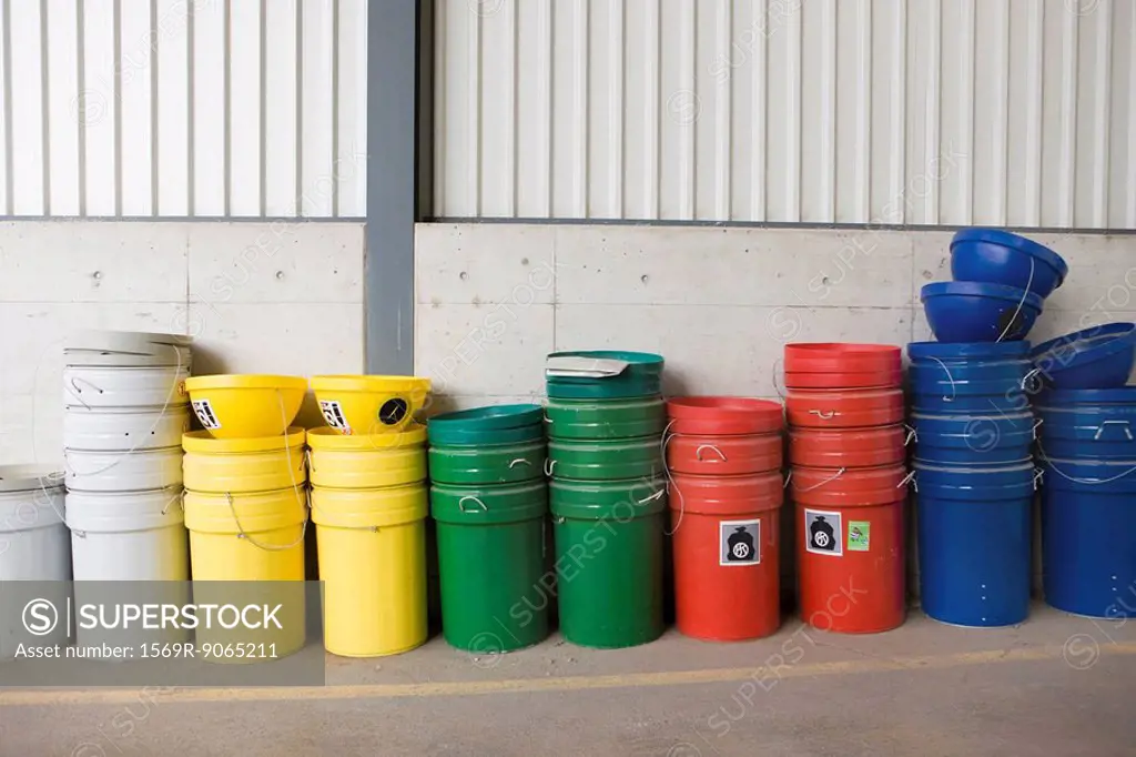 Multicolored garbage cans and recycling bins stacked along wall