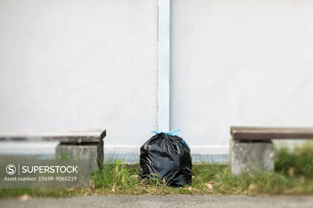 Garbage bag sitting on ground between two benches