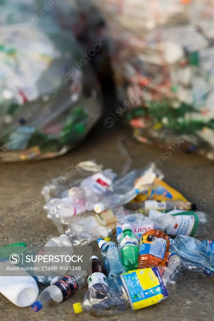 Crushed plastic bottles on ground, garbage bags in background