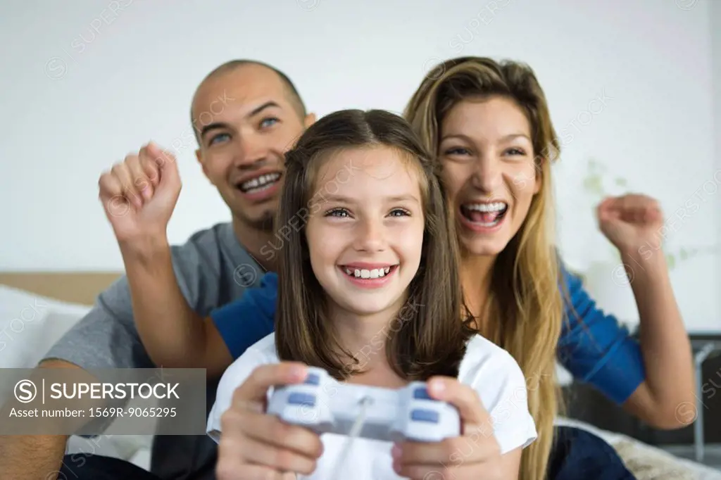 Girl playing video game, parents watching and cheering