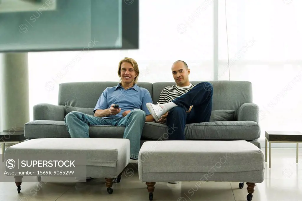 Two men sitting on sofa watching television