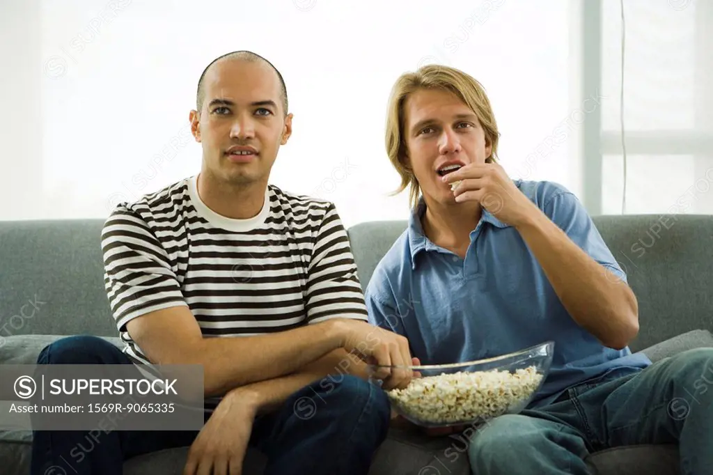 Two men sitting on sofa eating popcorn
