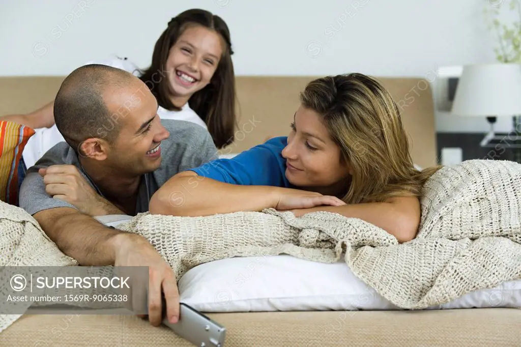 Family relaxing on bed together, man and woman smiling at each other