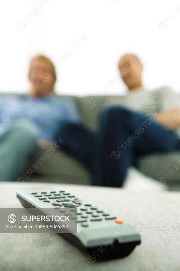 Close-up of remote control, men sitting on sofa in background