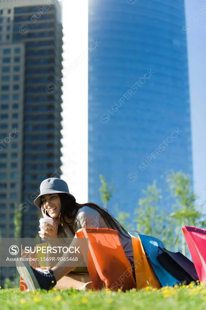 Young woman sitting in park with shopping bags, sipping drink with straw