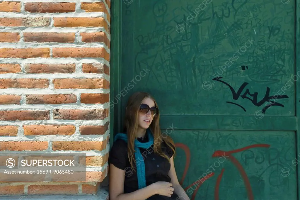Young woman in sunglasses leaning against wall
